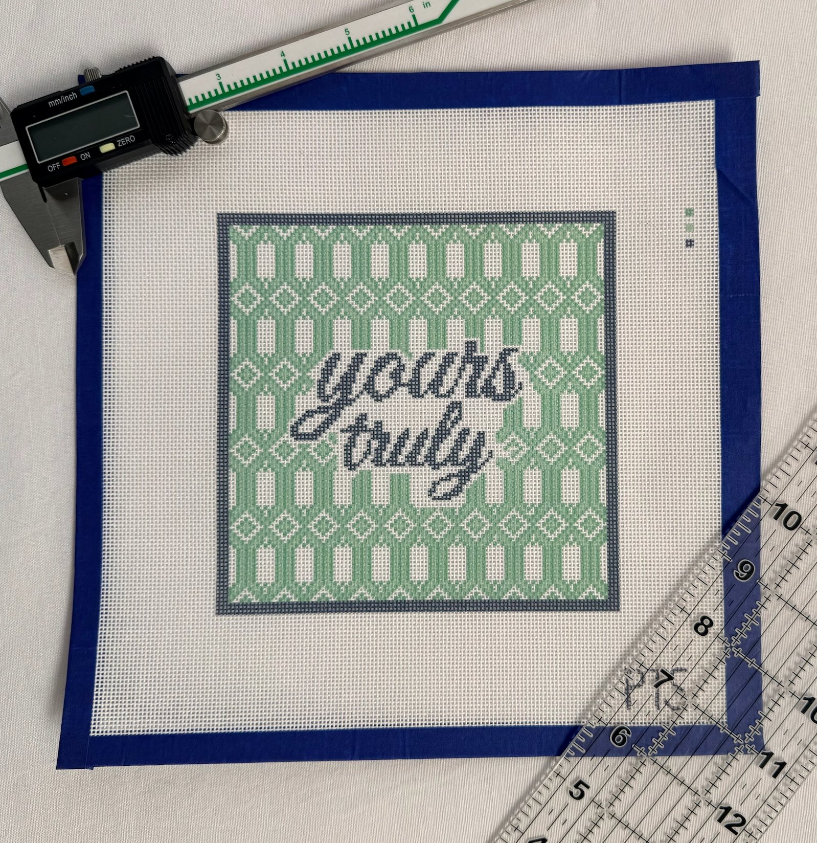 A printed yours truly canvas — navy script over a green trellis, taped and ready to stitch